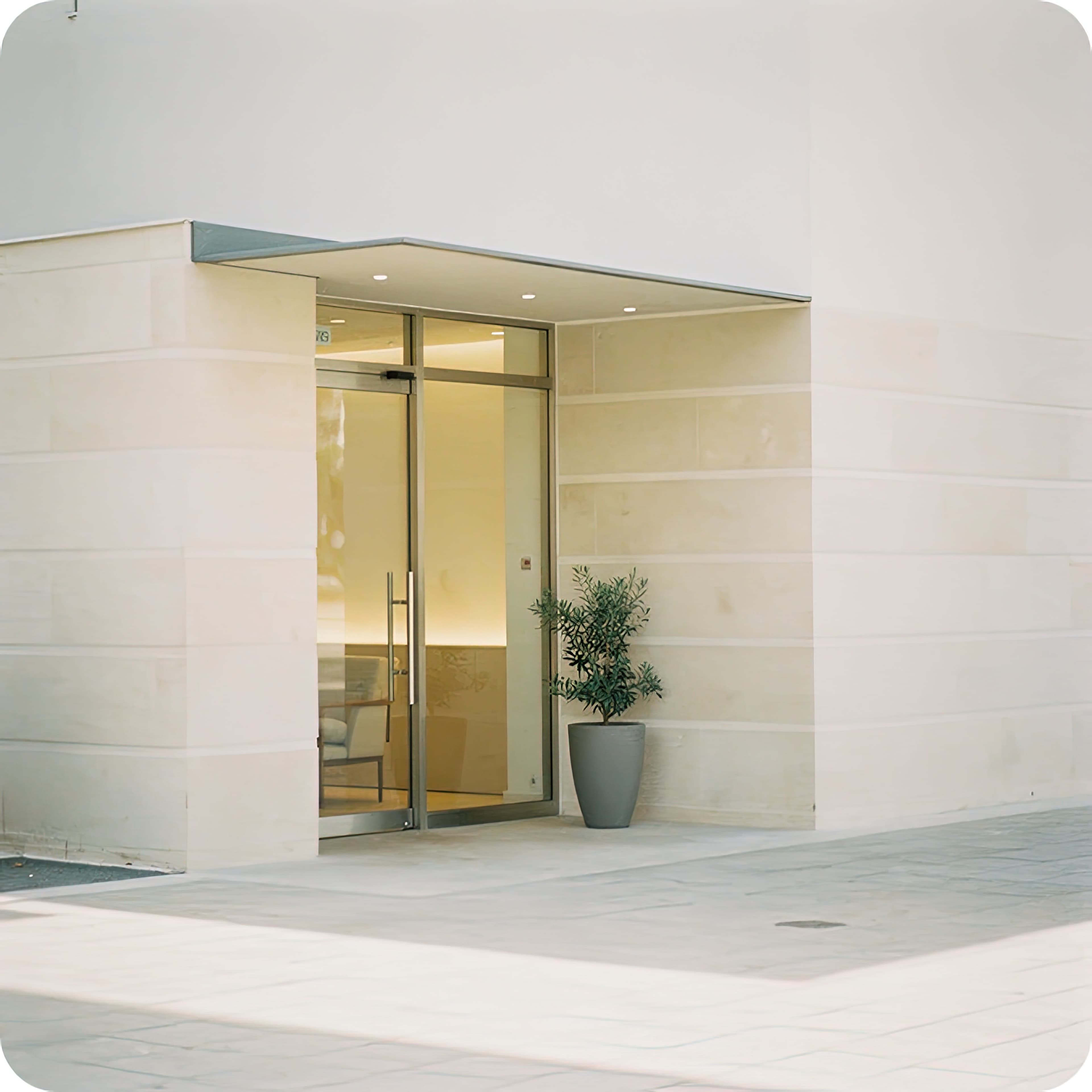 Stone building entrance with glass doors and a potted plant, representing accommodation