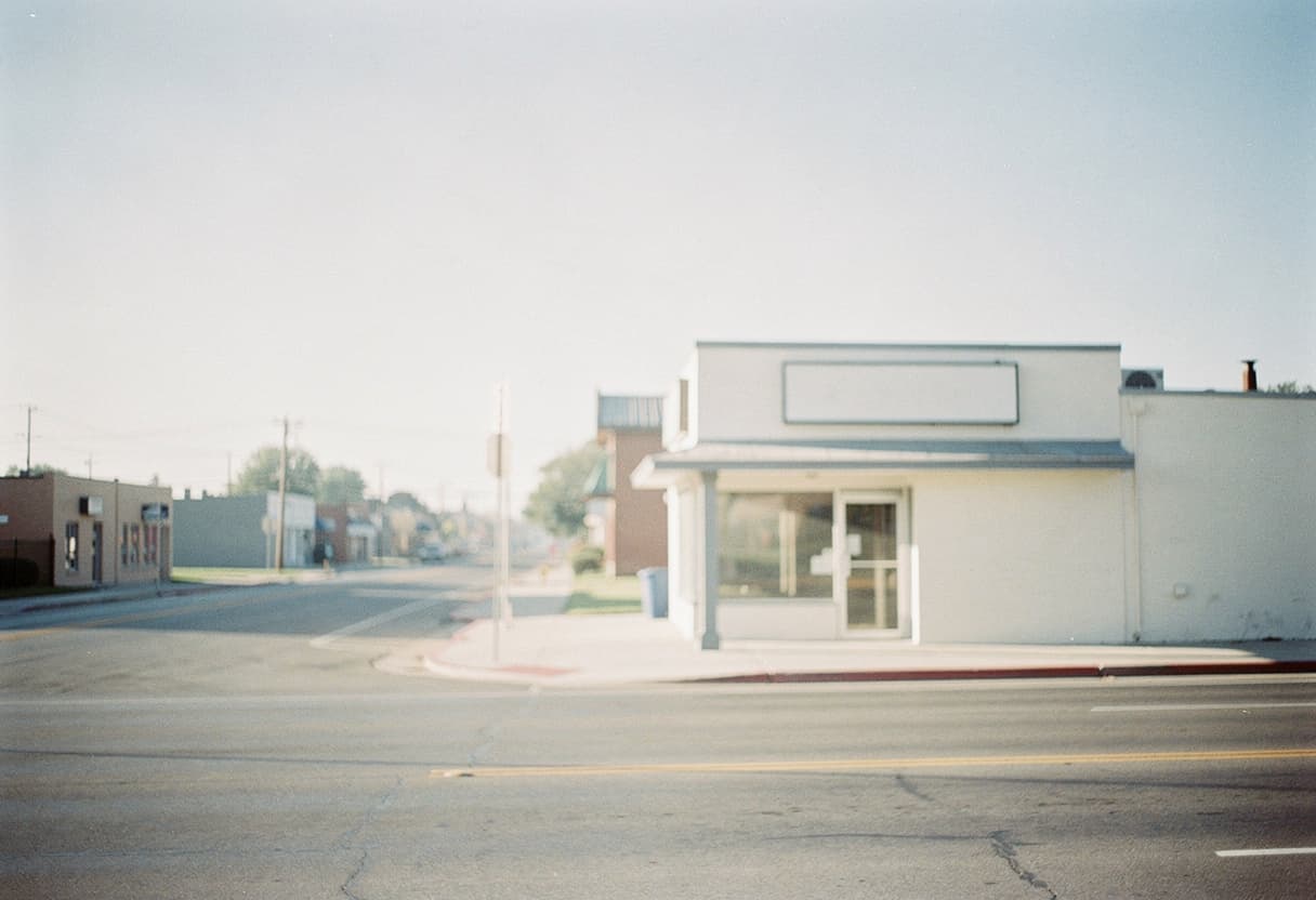 A quiet small-town street corner with a single-storey shop whose sign is blank